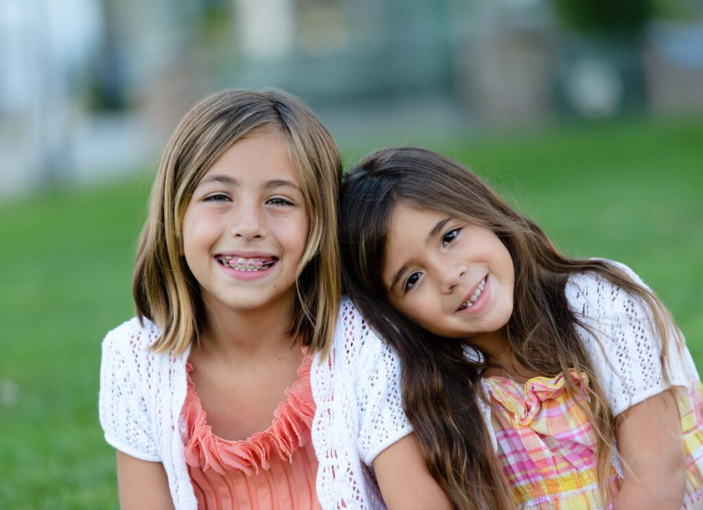 Small girl resting her shoulder on her friend who has pink braces for kids