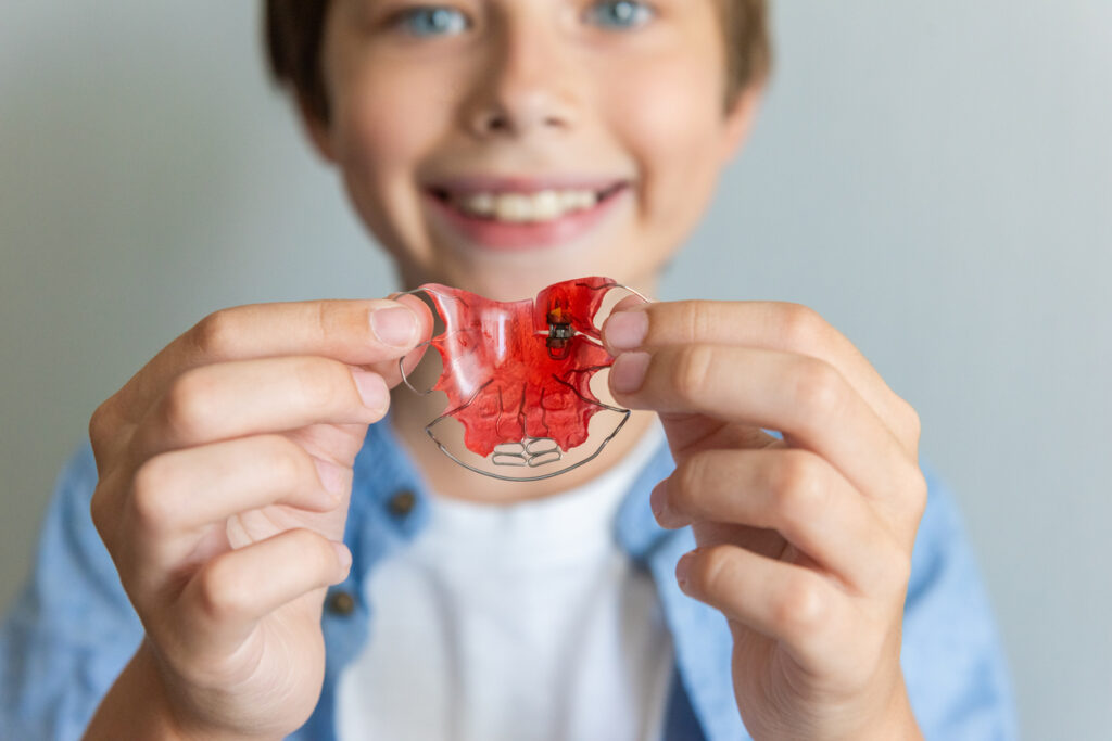Boy receiving early orthodontic treatment with palatal expanders holding them in front of him