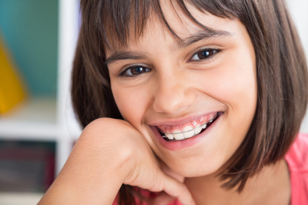 Girl with a removable retainer smiling while resting her chin on her hand