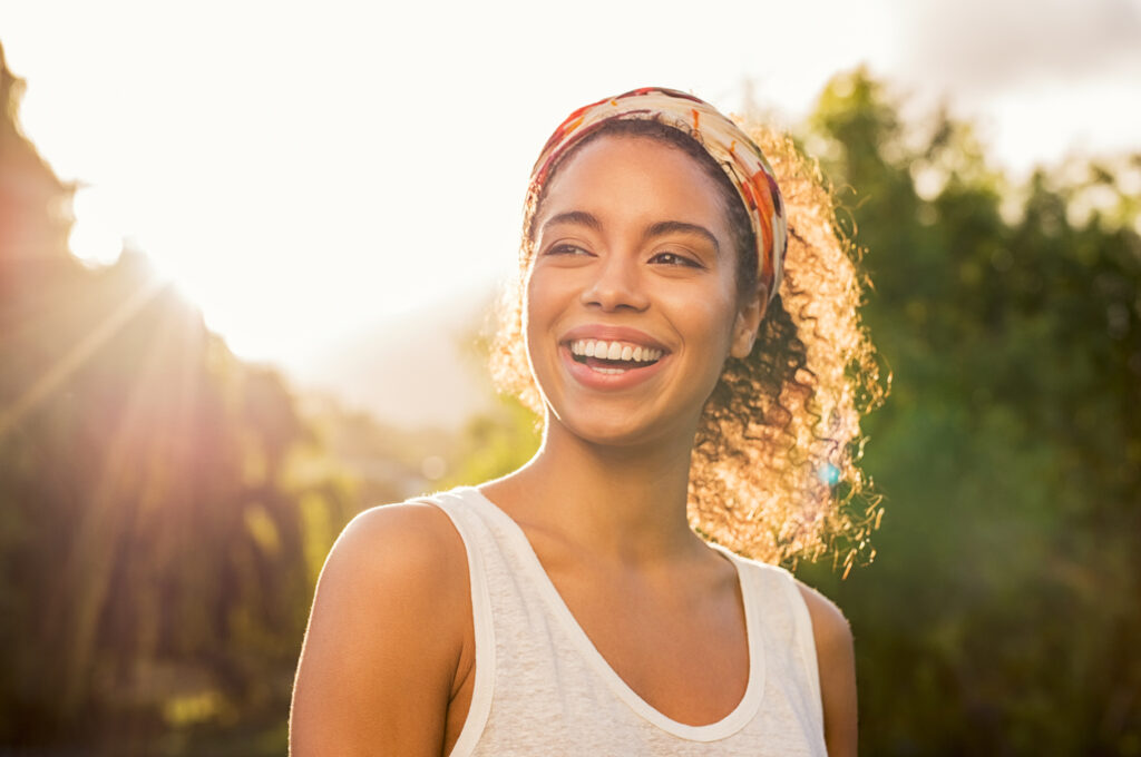 Close up of a woman with a glowing, aligned, smile in the summer sun